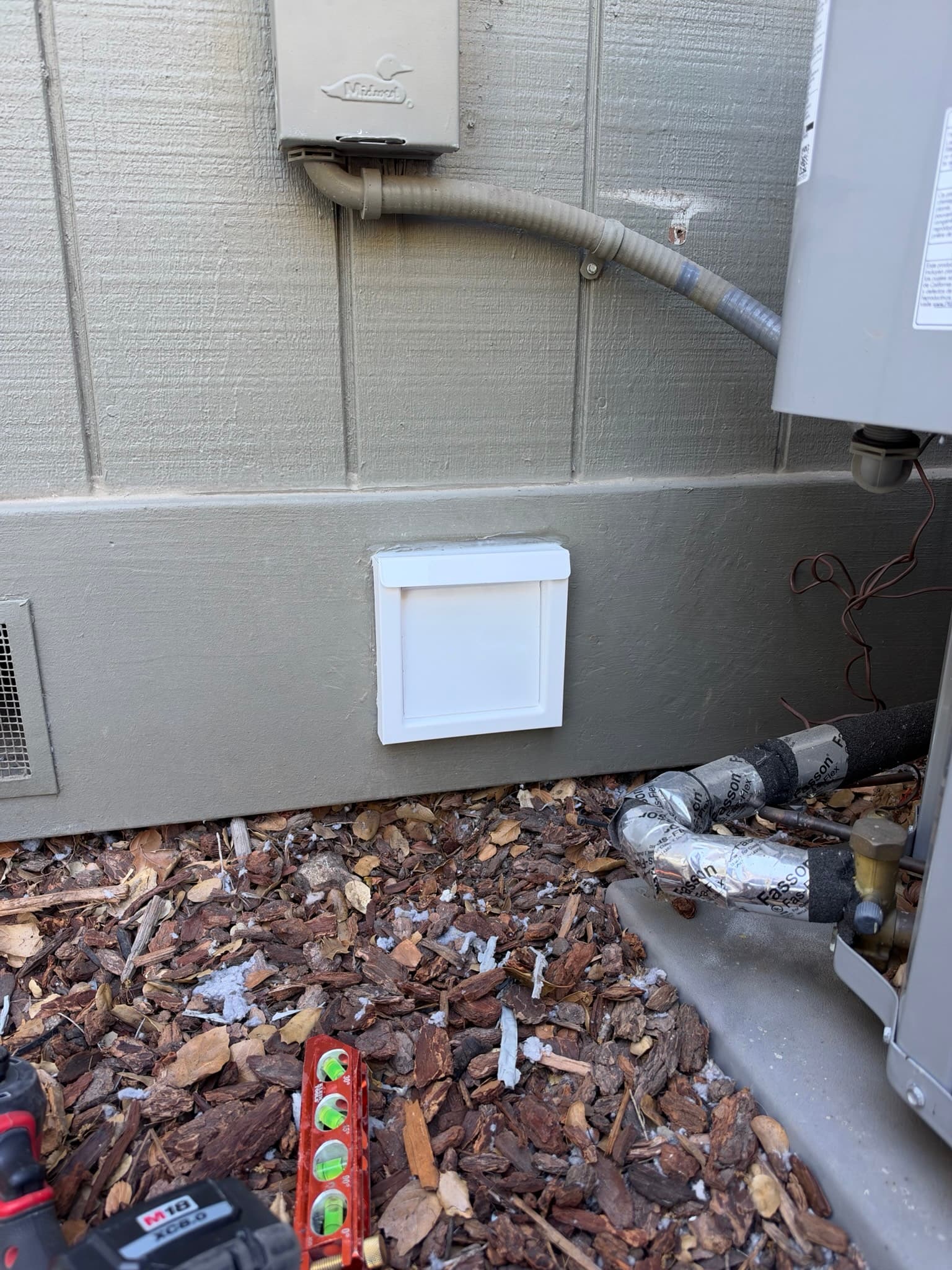 Newly installed white flush mount dryer wall vent sitting flush against painted siding with its gravity damper closed