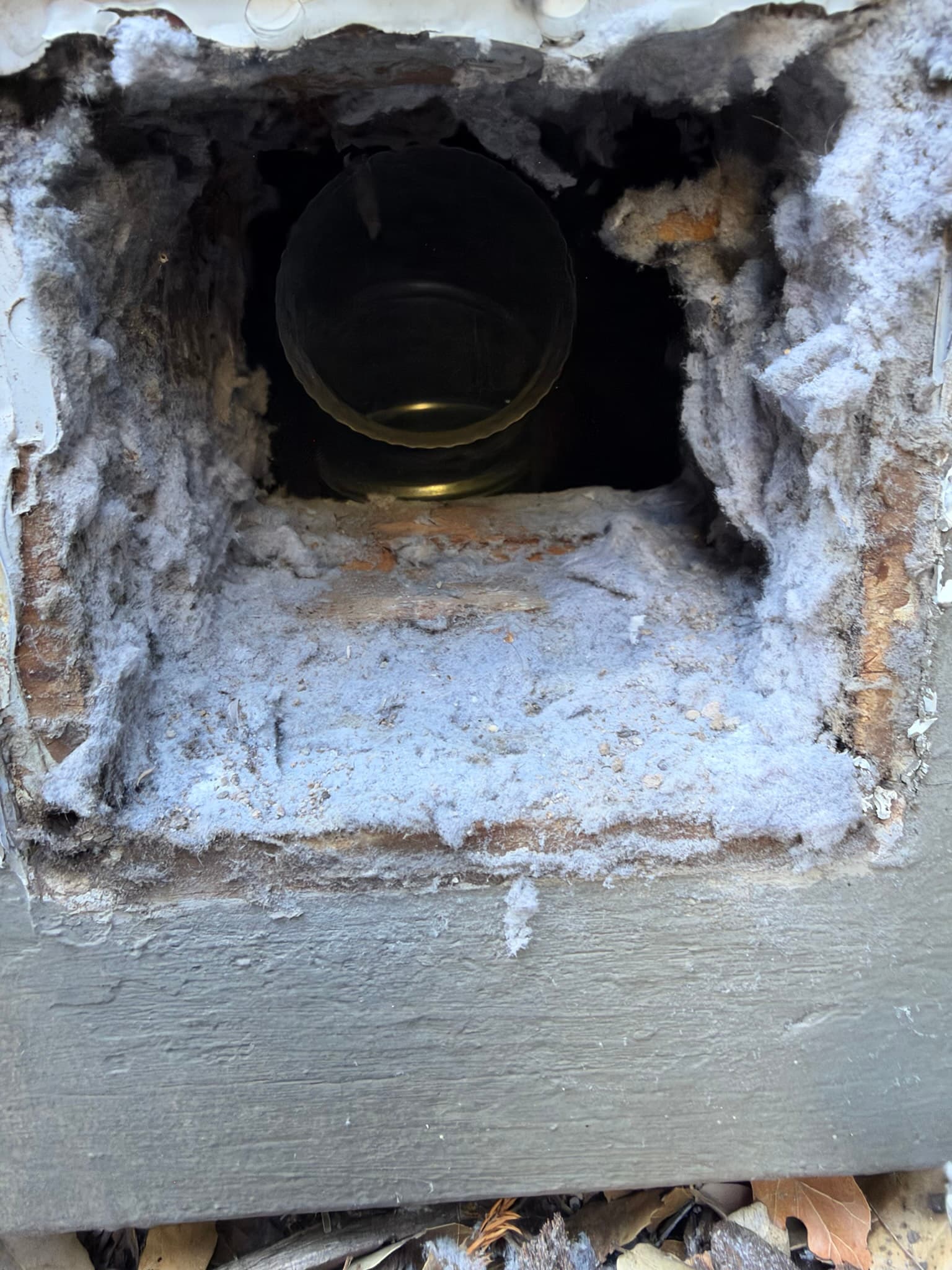 Exterior wall opening showing a metal duct terminal packed with heavy lint accumulation and no vent cap or hood installed