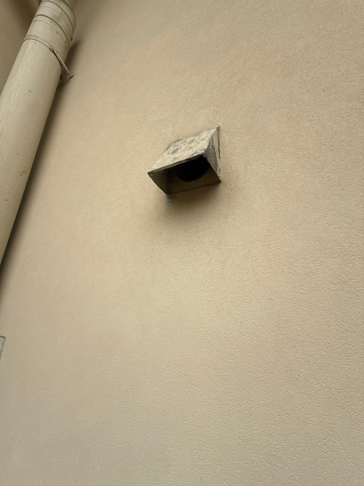 Exterior dryer vent hood mounted on a home in San Francisco, showing the cap in fair physical condition but missing the interior backdraft damper flap, making the installation non-compliant with IRC M1502.3