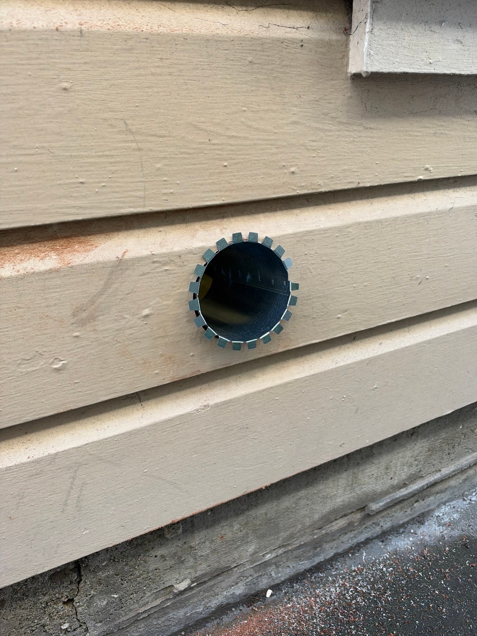 Freshly cut round opening through exterior wood siding in San Francisco with a rough-in metal collar exposing the bare duct interior, prior to wall vent installation
