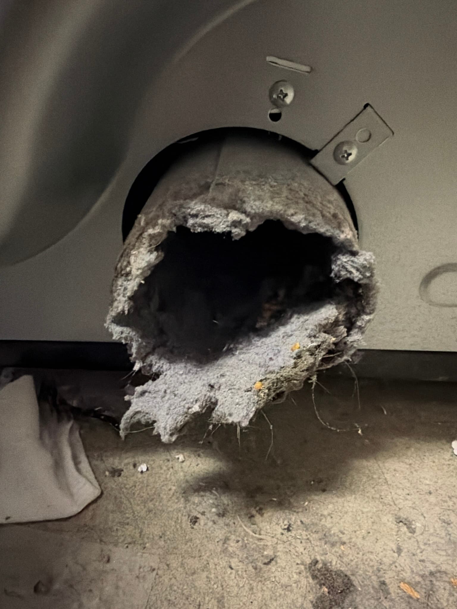 Dryer's rear exhaust port packed with a thick, matted ring of lint almost completely blocking the opening before cleaning