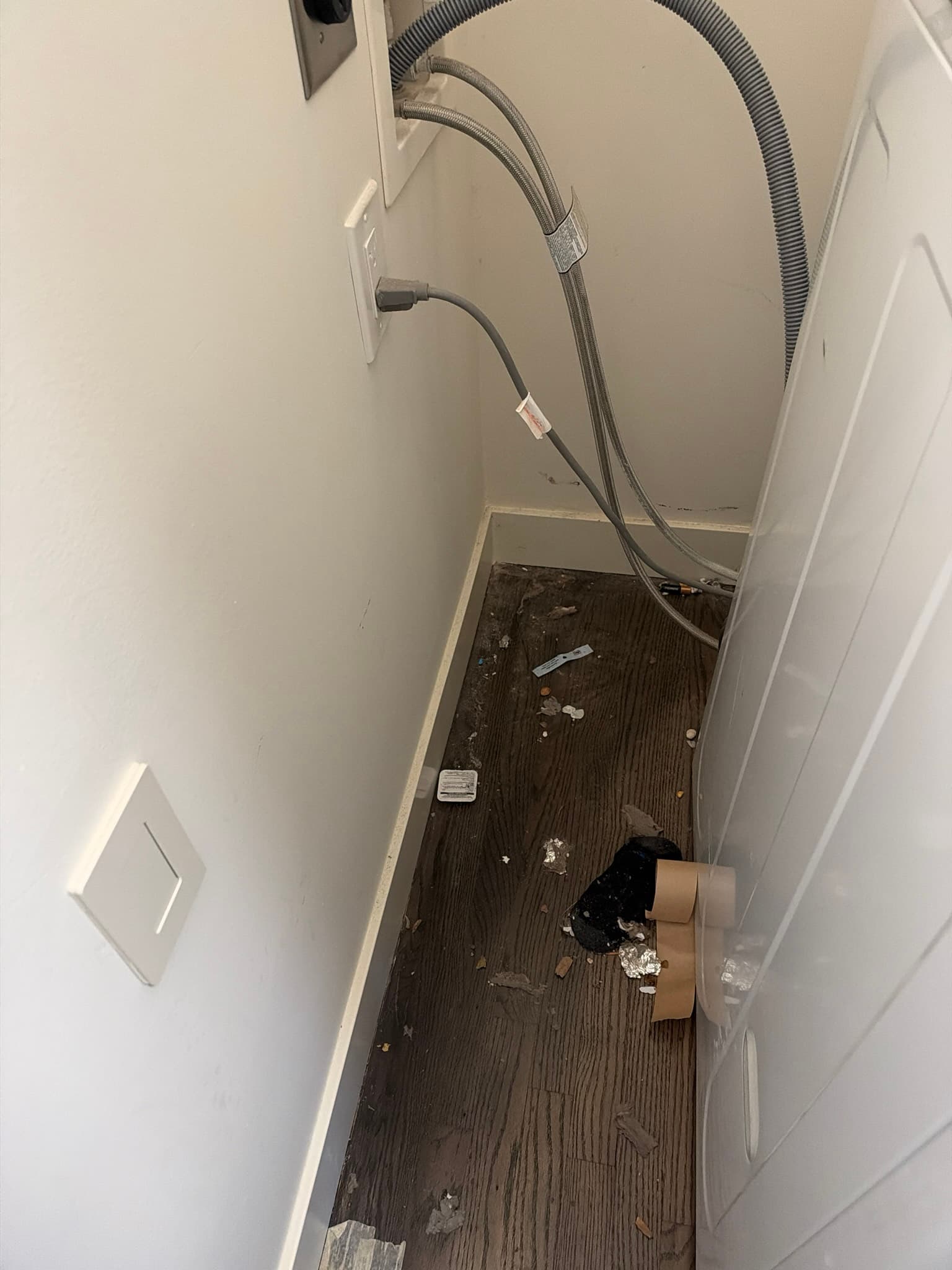 Space behind a pulled-out washer and dryer showing the old flexible transition duct and braided washer supply lines before service