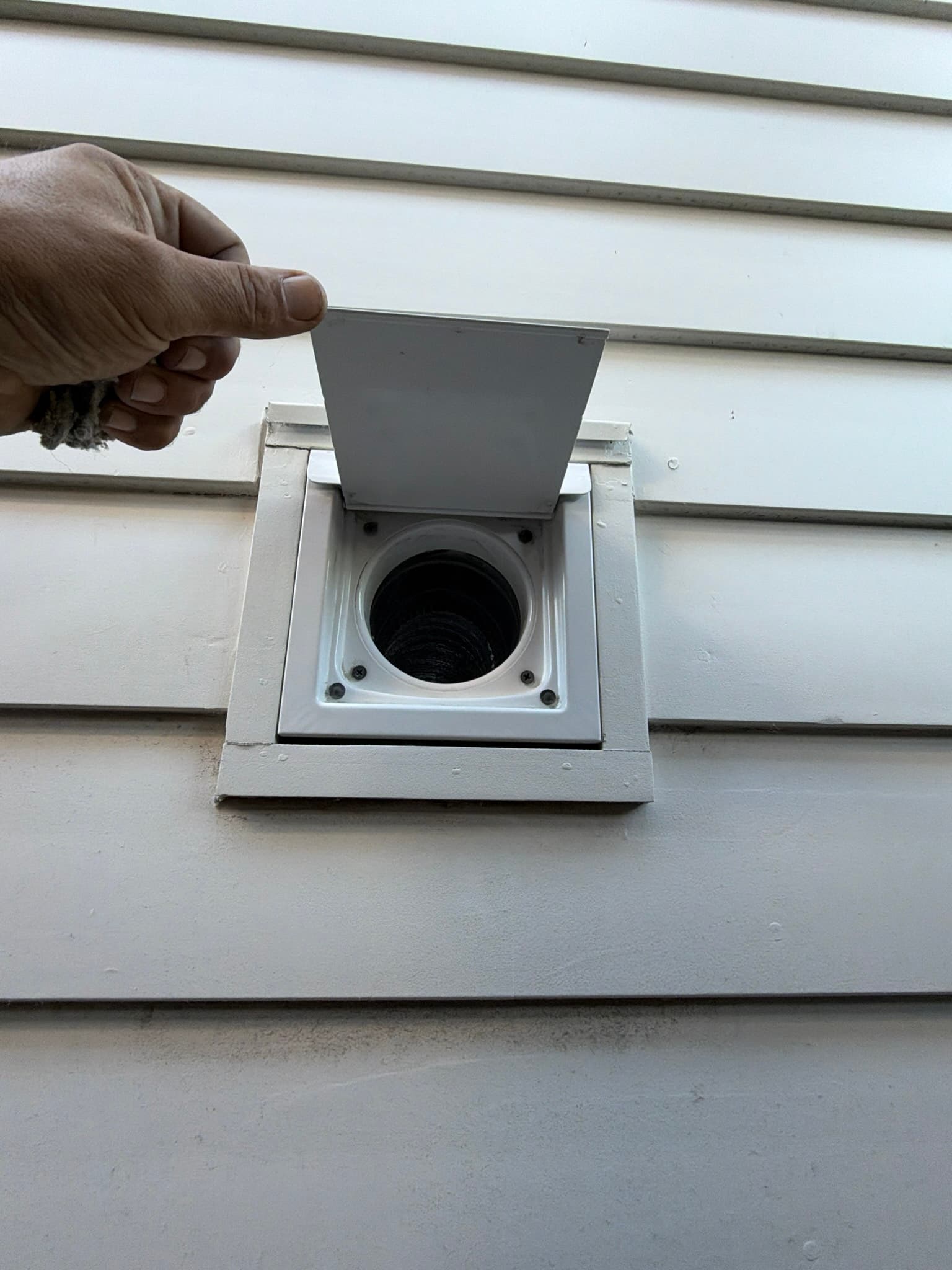 Close-up view of the exterior dryer vent housing set into vinyl siding
