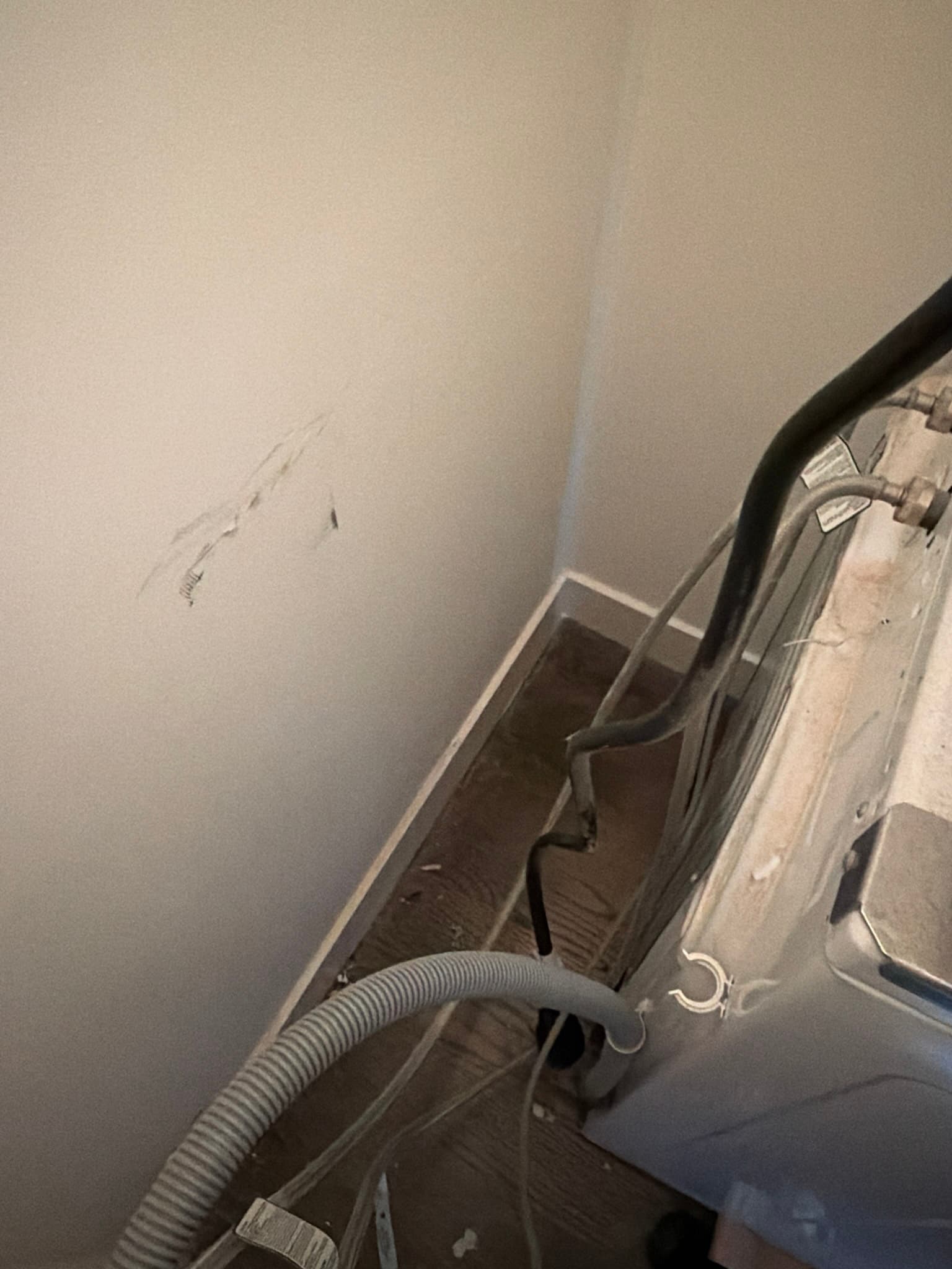 Rear of the laundry area with washer supply hoses, drain line, and electrical cords visible behind the pulled-out units