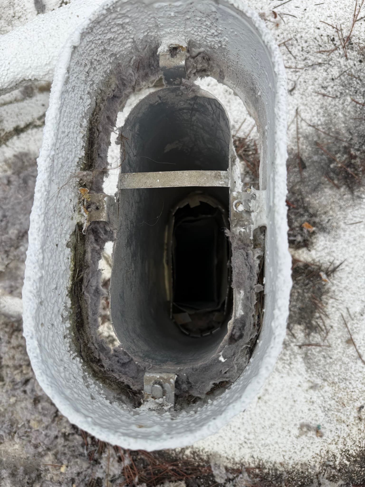Exterior dryer vent cap with a rigid metal duct interior caked in lint and debris, the flapper door appearing damaged or stuck partially open