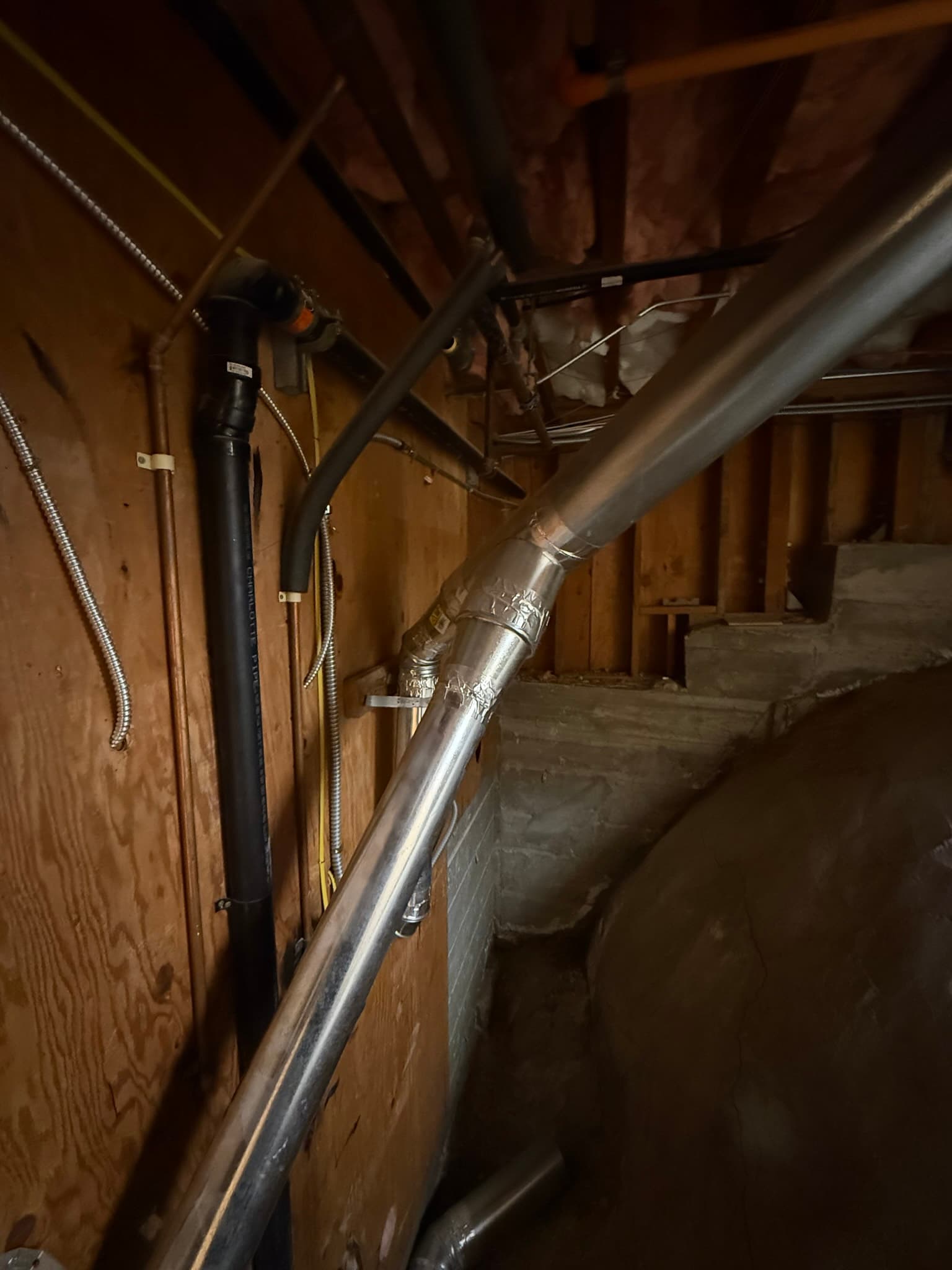 Attic space with new rigid metal dryer vent duct running diagonally across wooden framing, joints sealed with metal foil tape, with flexible metal conduits routed alongside