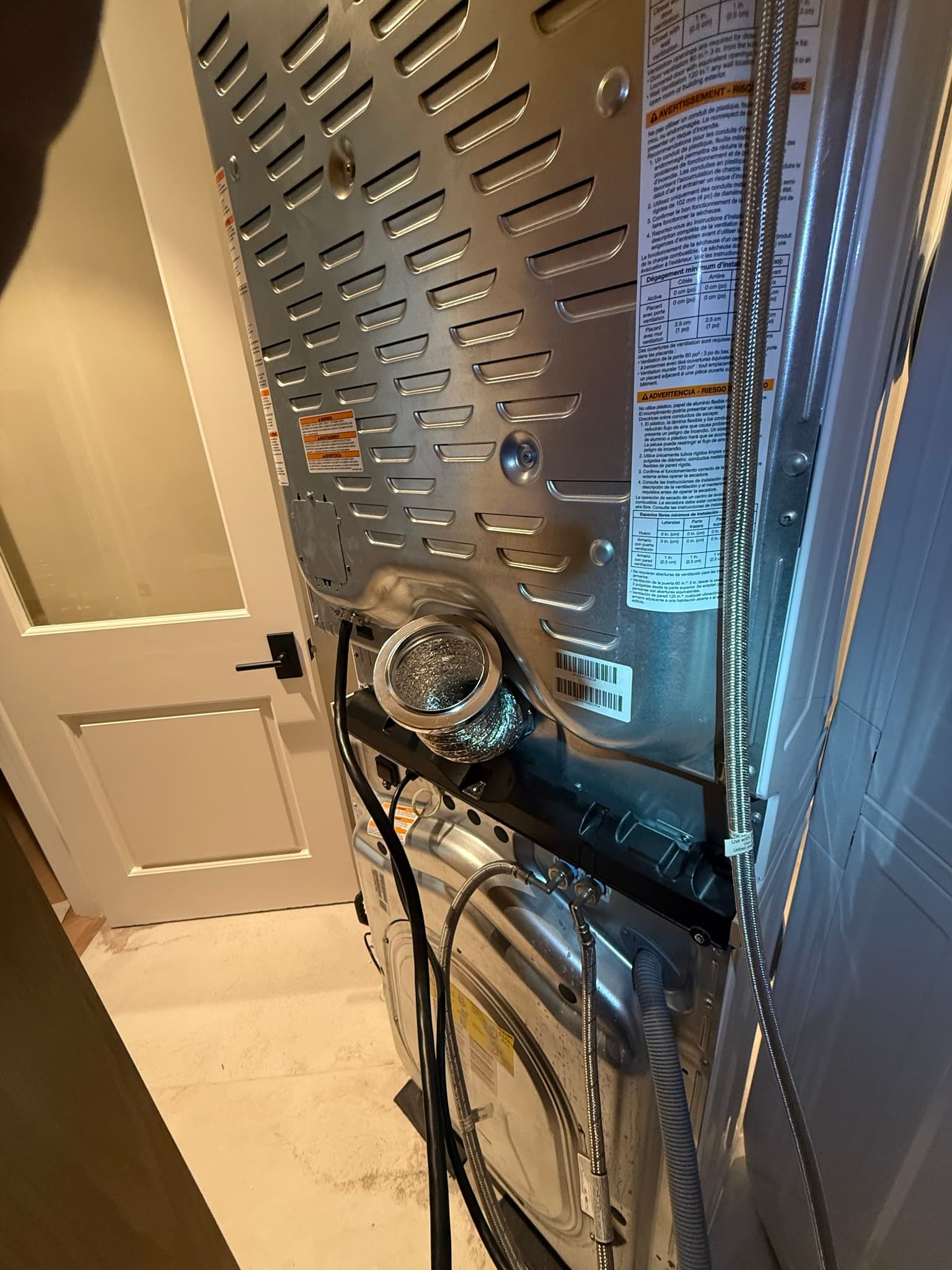 Rear of a stacked laundry unit showing the MagVent 12-inch transition duct and magnetic ring connected to the dryer exhaust outlet, with lint accumulation visible at the connection point prior to cleaning
