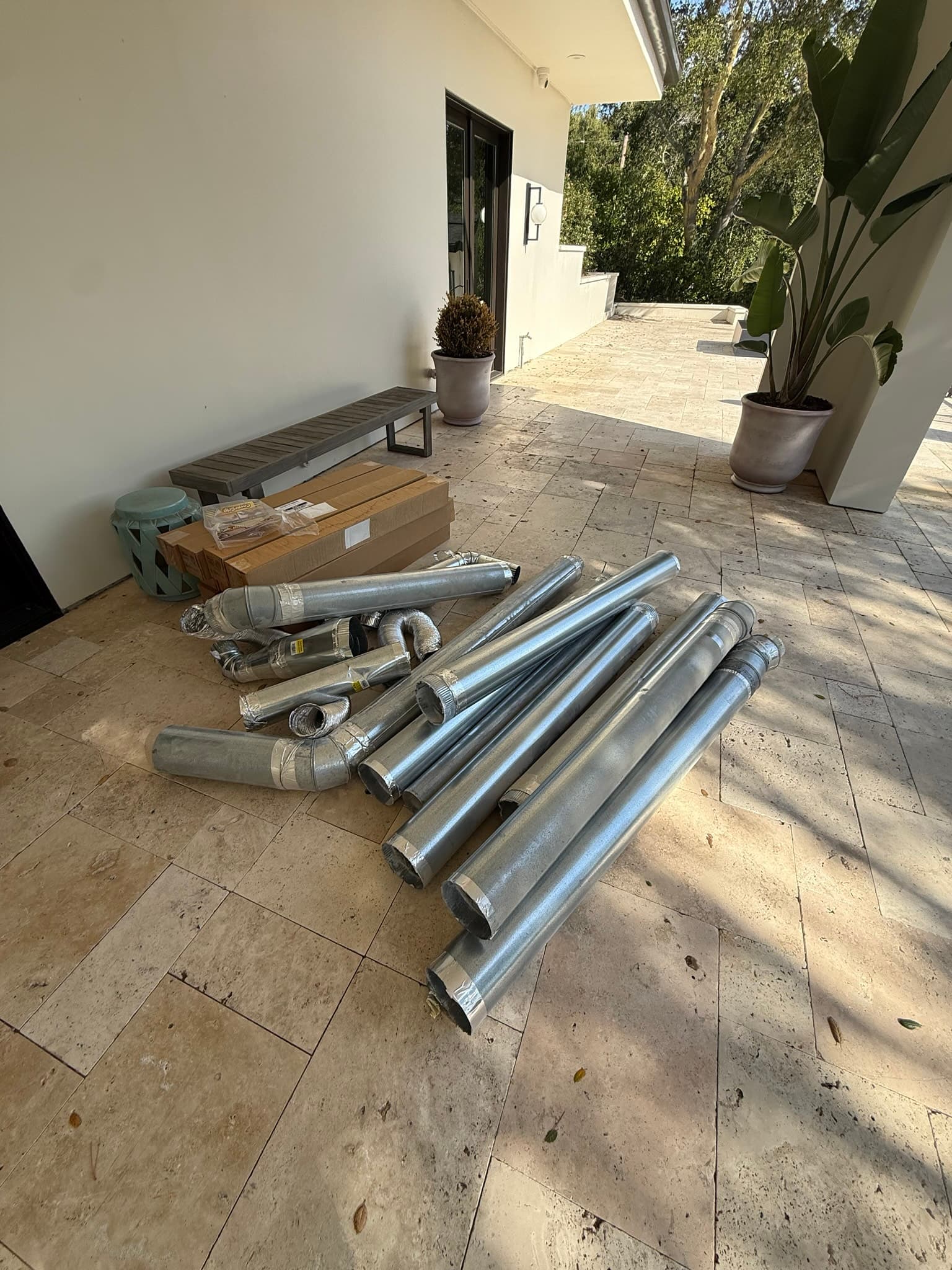 Removed sections of old 6-inch-diameter rigid metal dryer duct laid out on a patio, including multiple elbows, taped connectors, and a periscope-style cap, representing approximately 60 feet of non-compliant ductwork