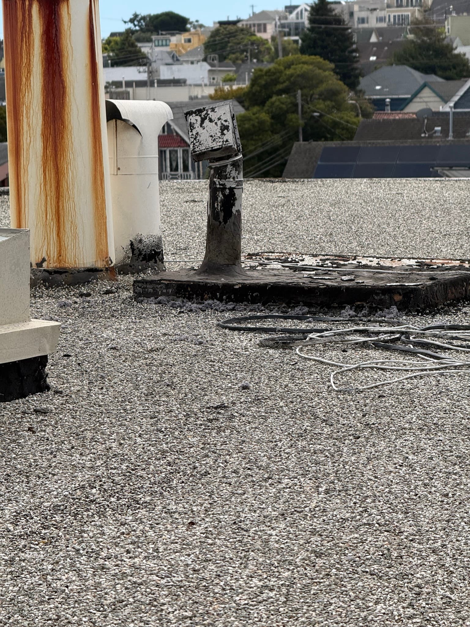 Rooftop dryer vent periscope-style cap showing heavy corrosion, blackening, and rust on its exterior metal box, with flexible ductwork appearing disconnected or improperly secured in the foreground and water-stained wood framing to the left