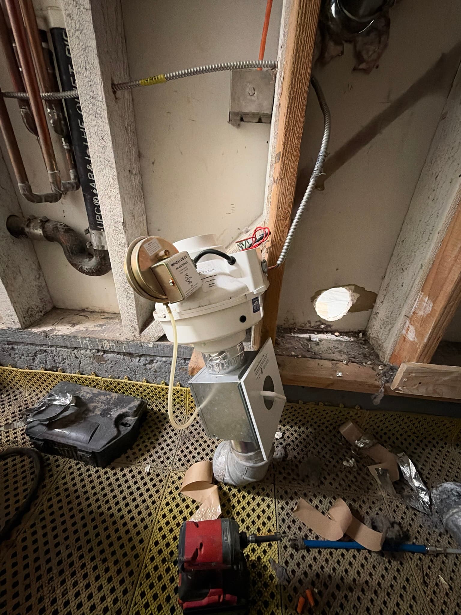 Inline booster fan mounted in an open wall cavity and connected to the metal ductwork via a transition box, prior to its removal during the duct repair