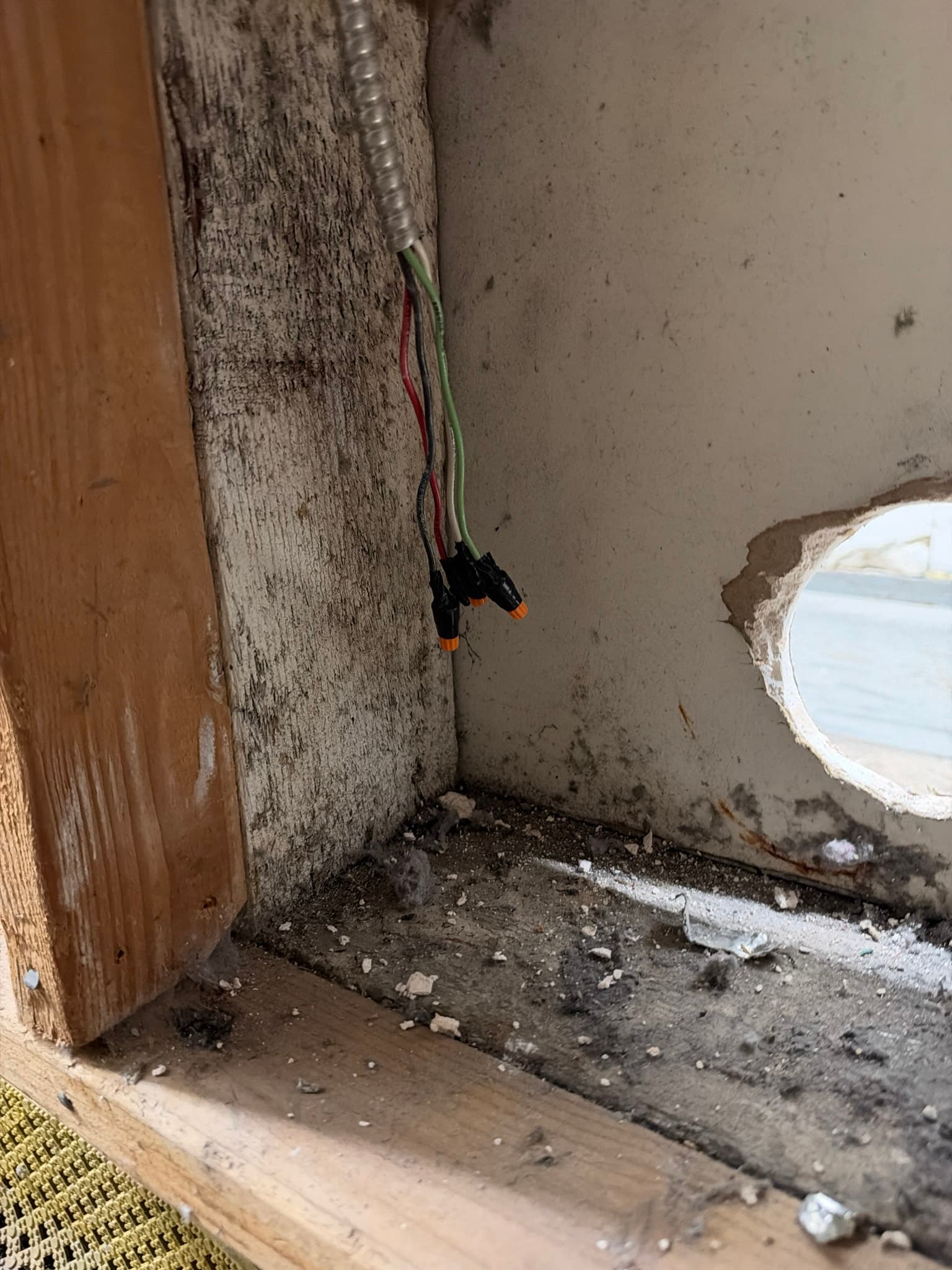 Interior wall cavity coated in heavy dust and lint accumulation along the framing and floor, with wiring and a section of flexible metal duct running through the space prior to cleaning