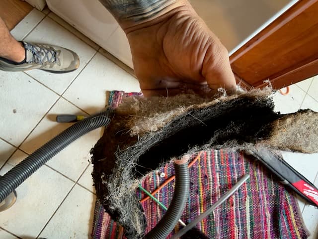 Technician holding a thick felted slab of compacted gray and black lint pulled from a residential dryer exhaust system